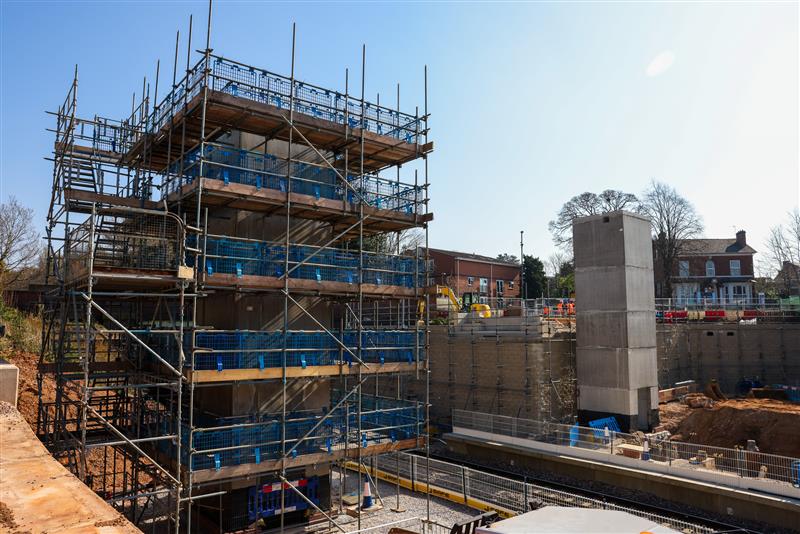 The station construction site with rail line flanked by two concrete towers, set to become the footbridge and lifts.