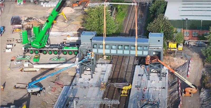Picture from above shows large green crane with box bridge dangling below above the rail tracks