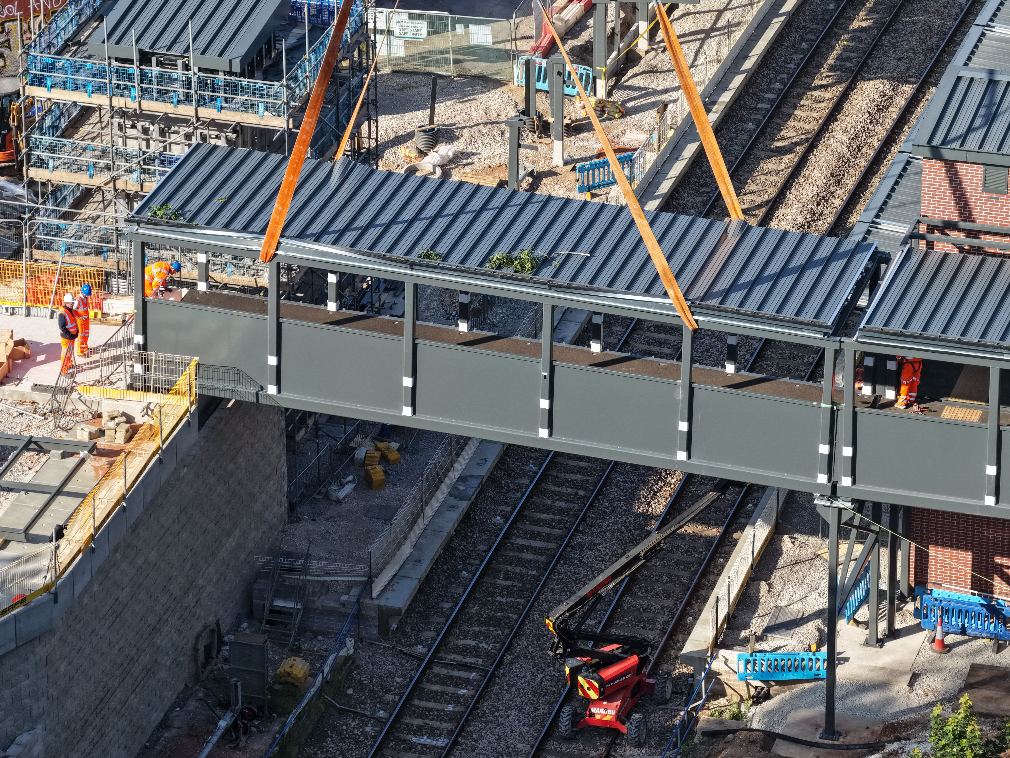 A giant box bridge suspended from straps is being lowered onto blocks either side of the railway line - daylight picture