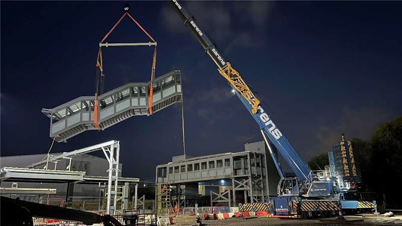 A night a box stairway is dangling from a large crane over the construction site